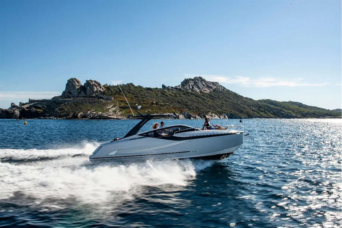 A sleek white motorboat speeds across sparkling water near rocky hills, with passengers enjoying the scenic ride.